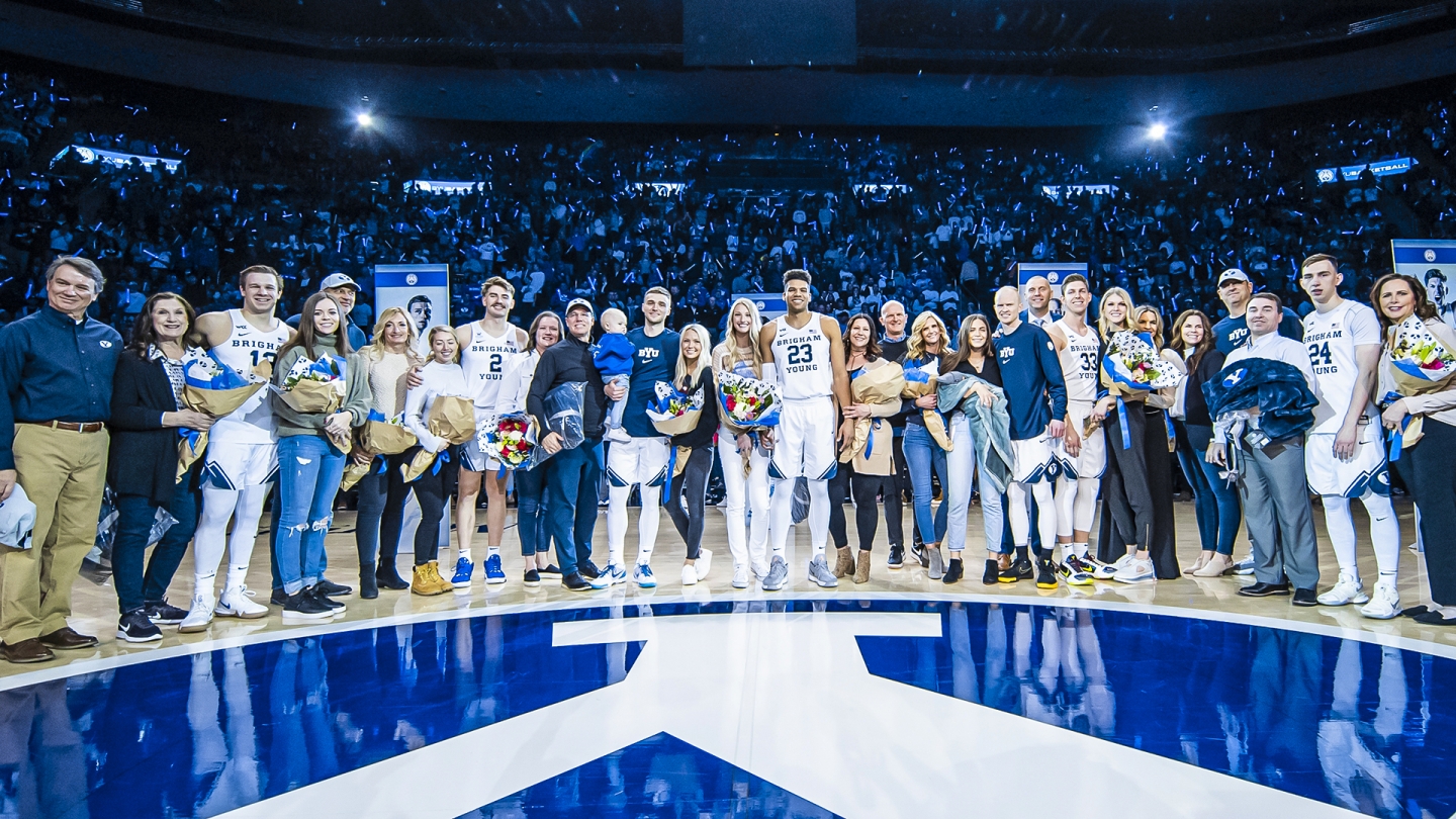 BYU men's basketball's seniors with their families standing at center court in the Marriott Center.