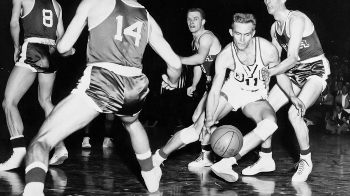 Roland Minson dribbles the basketball between several Utah basketball players.