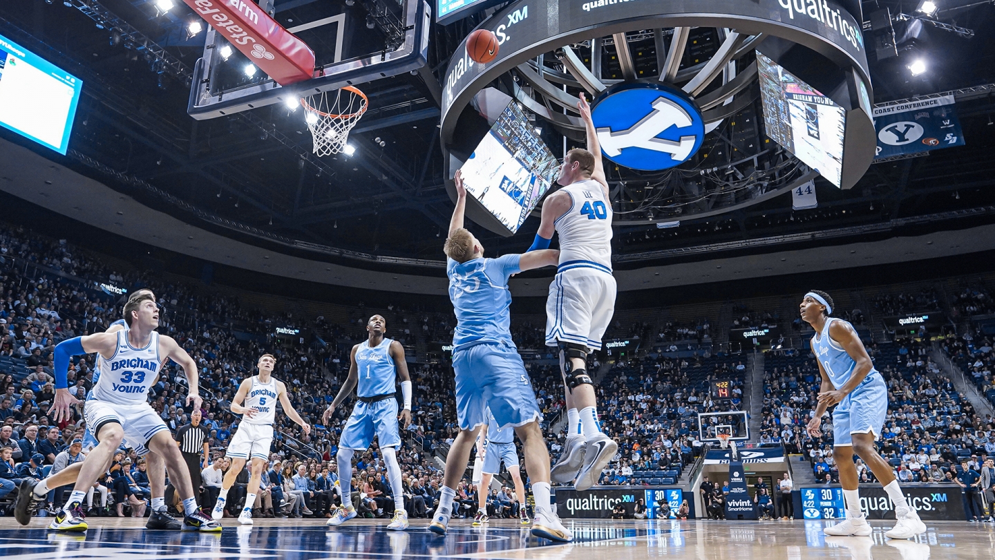 Kolby Lee shoots a hook shot from the baseline on the left side of the basket while several players look on.